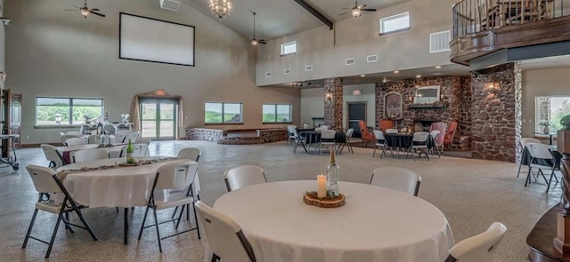 dining space featuring beam ceiling, high vaulted ceiling, ceiling fan, and a stone fireplace