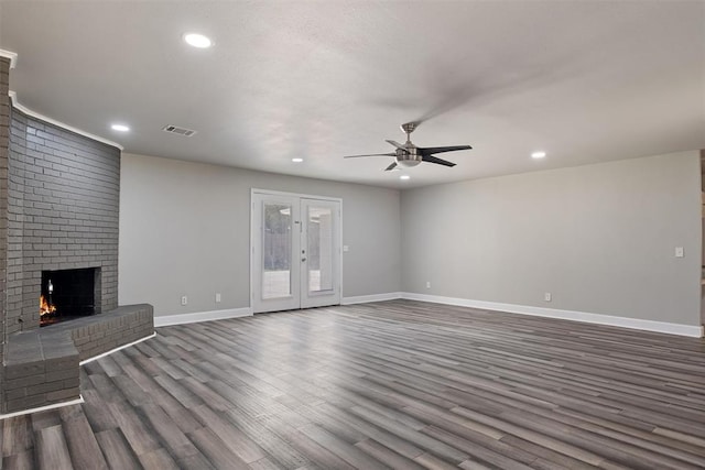 unfurnished living room with a fireplace, ceiling fan, dark hardwood / wood-style flooring, and french doors