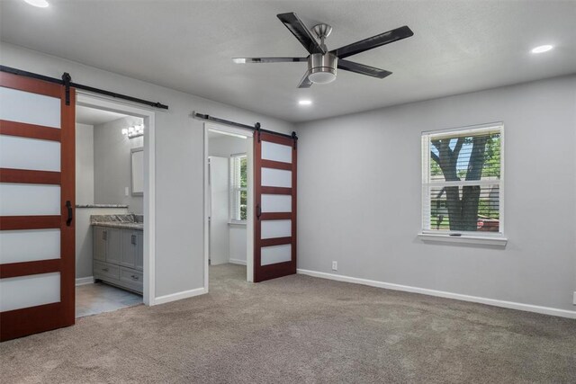 unfurnished bedroom featuring connected bathroom, a barn door, ceiling fan, and light carpet