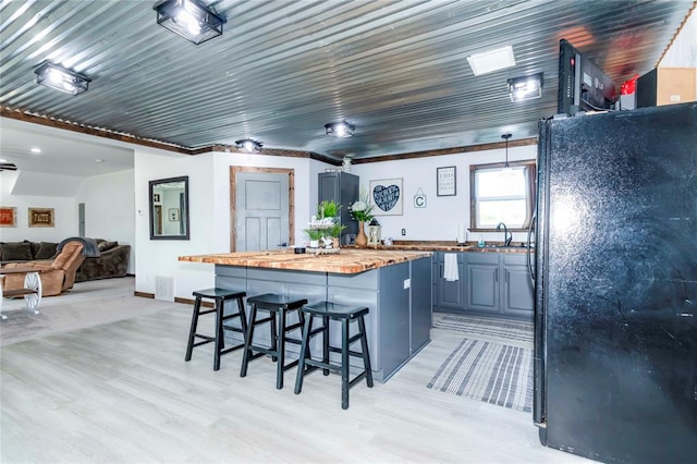 kitchen featuring wood counters, black refrigerator, hanging light fixtures, light wood-type flooring, and a breakfast bar area