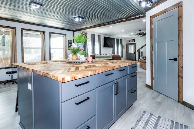 kitchen with a center island, ceiling fan, light wood-type flooring, butcher block counters, and a breakfast bar area