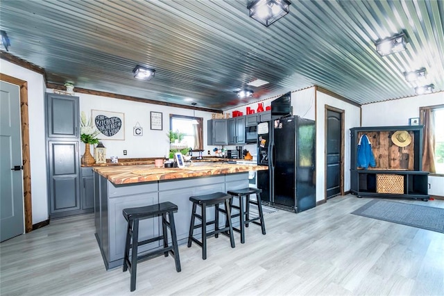 kitchen featuring black appliances, a breakfast bar, light wood-type flooring, and butcher block counters