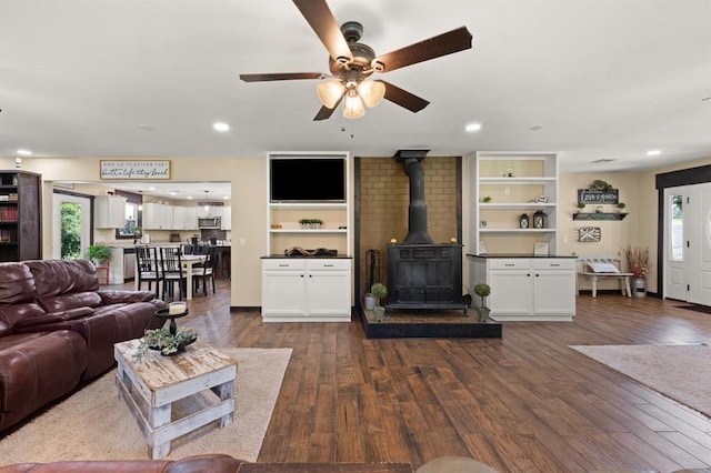 living room featuring a wood stove, built in shelves, and dark hardwood / wood-style floors