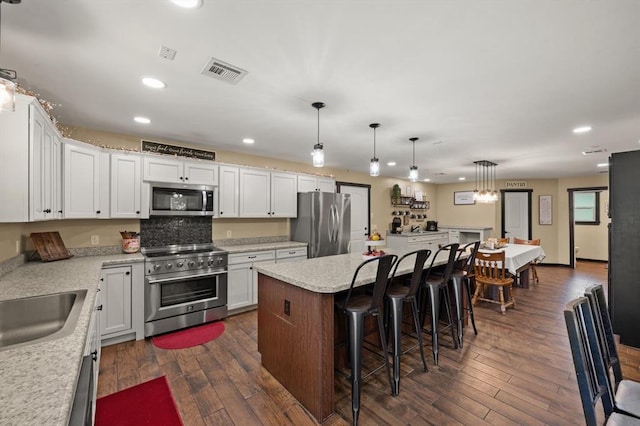 kitchen featuring stainless steel appliances, white cabinets, a center island, dark hardwood / wood-style floors, and hanging light fixtures