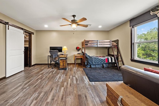 bedroom with a barn door, ceiling fan, and wood-type flooring