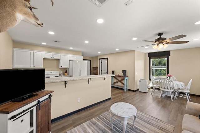 kitchen featuring a kitchen bar, white appliances, white cabinets, and dark wood-type flooring