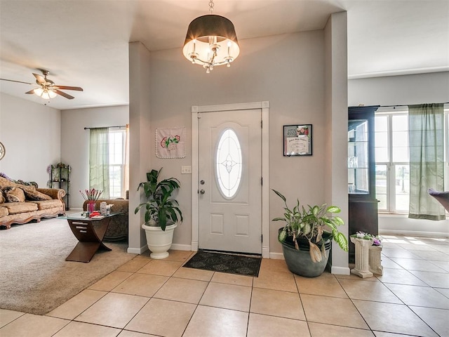 tiled entrance foyer with a healthy amount of sunlight and ceiling fan with notable chandelier