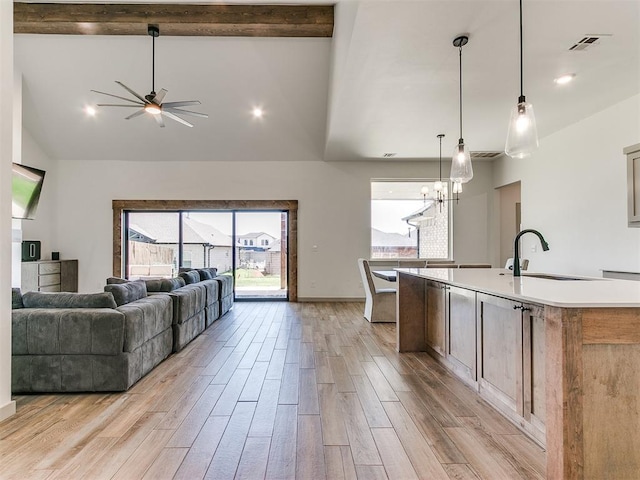 kitchen featuring light wood-type flooring, ceiling fan with notable chandelier, sink, pendant lighting, and an island with sink