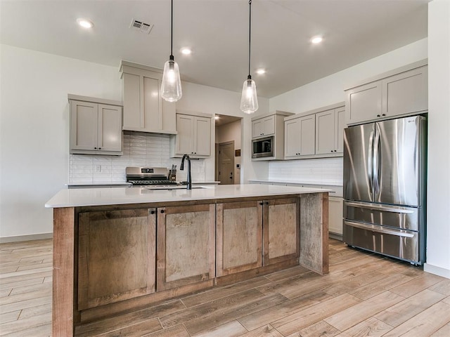 kitchen with pendant lighting, a center island with sink, sink, light hardwood / wood-style flooring, and appliances with stainless steel finishes