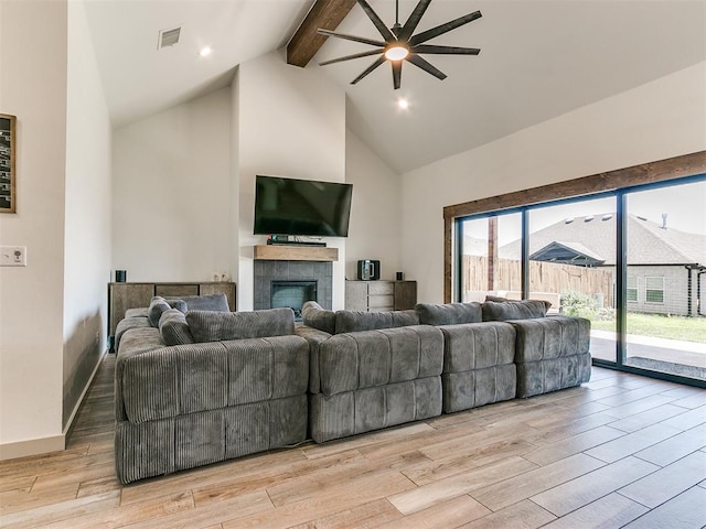 living room with ceiling fan, light hardwood / wood-style flooring, beamed ceiling, high vaulted ceiling, and a tiled fireplace