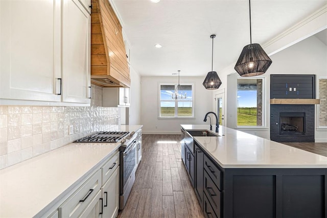 kitchen with stainless steel range with gas cooktop, a sink, light countertops, dark wood-type flooring, and tasteful backsplash