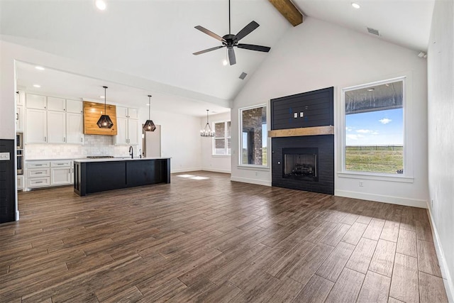 unfurnished living room with beamed ceiling, high vaulted ceiling, ceiling fan with notable chandelier, a fireplace, and dark wood-style flooring