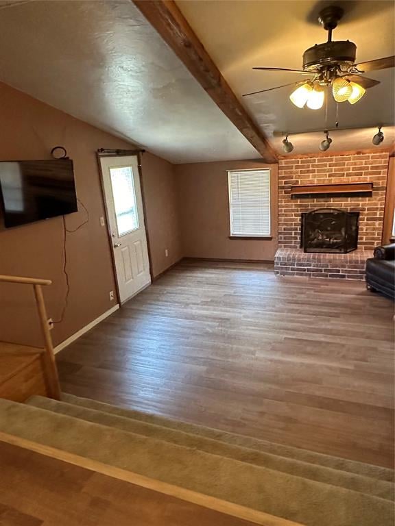 unfurnished living room with beamed ceiling, ceiling fan, wood-type flooring, and a fireplace