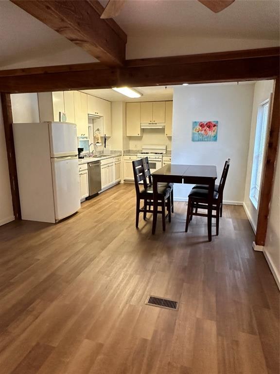 dining space featuring beamed ceiling, light wood-type flooring, and sink