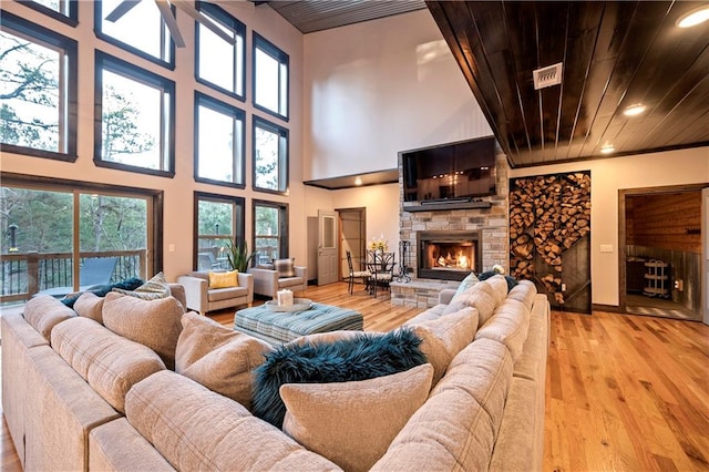 living room featuring a fireplace, a towering ceiling, light wood-type flooring, and plenty of natural light