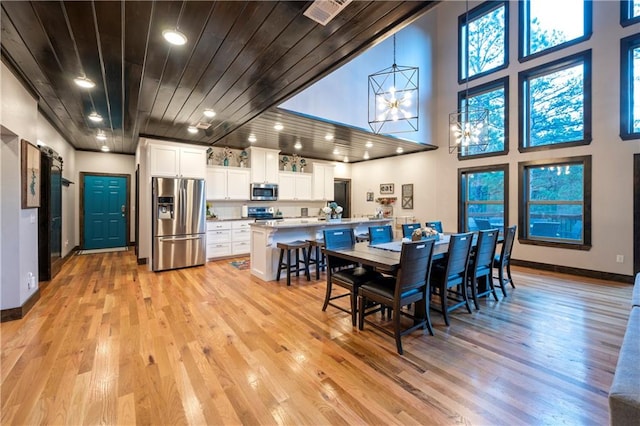 dining room with wooden ceiling, a towering ceiling, and light hardwood / wood-style floors