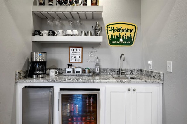 bar with stainless steel refrigerator, sink, wine cooler, light stone counters, and white cabinets