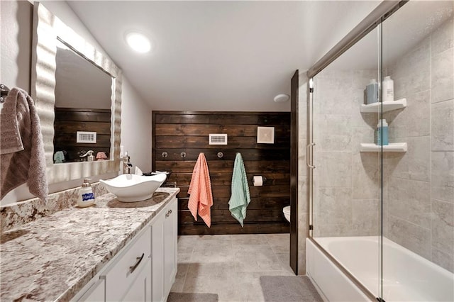 full bathroom featuring vanity, bath / shower combo with glass door, toilet, and wood walls