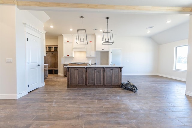 kitchen with white cabinets, hanging light fixtures, an island with sink, and vaulted ceiling