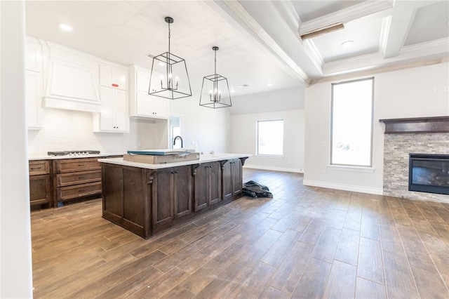 kitchen with white cabinetry, a fireplace, a center island with sink, pendant lighting, and beam ceiling