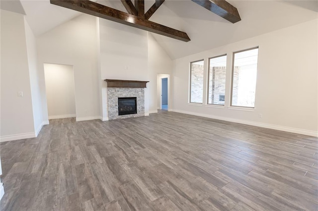 unfurnished living room featuring beamed ceiling, high vaulted ceiling, a stone fireplace, and hardwood / wood-style floors