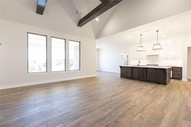 unfurnished living room with high vaulted ceiling, beam ceiling, light hardwood / wood-style floors, and sink