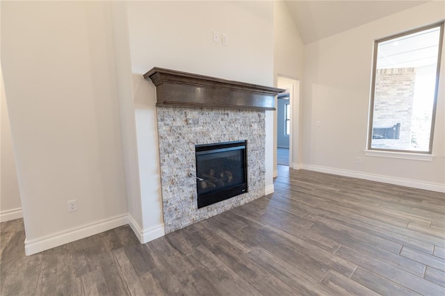 unfurnished living room featuring a stone fireplace, dark wood-type flooring, and vaulted ceiling