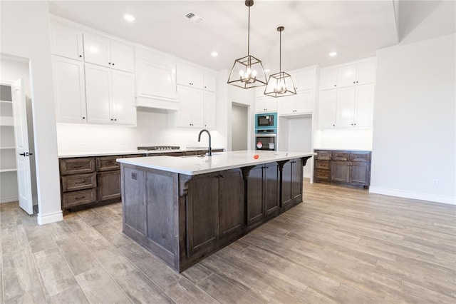 kitchen with pendant lighting, a kitchen island with sink, gas stovetop, built in microwave, and custom exhaust hood