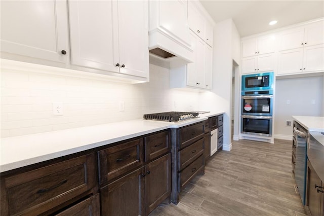 kitchen featuring white cabinets, decorative backsplash, dark brown cabinetry, light hardwood / wood-style floors, and stainless steel appliances