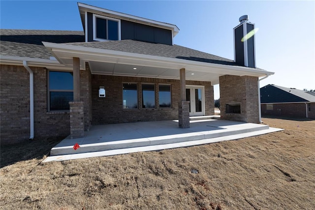 rear view of house featuring an outdoor brick fireplace and a patio area