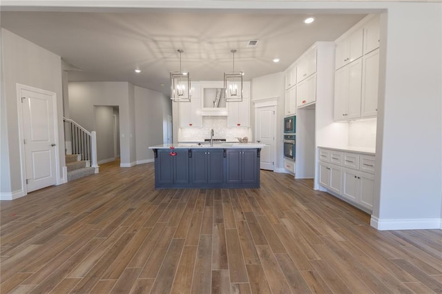 kitchen with white cabinets, an island with sink, hardwood / wood-style flooring, sink, and decorative light fixtures