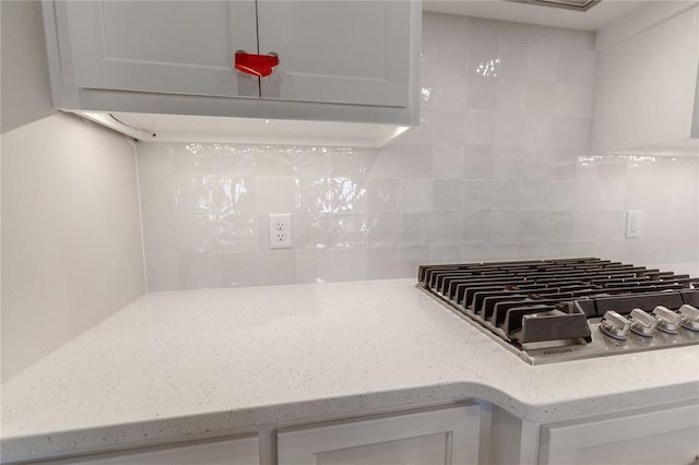 kitchen with stainless steel gas stovetop, white cabinetry, backsplash, and light stone counters