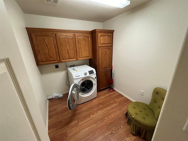 laundry area with cabinets, washer / dryer, a textured ceiling, and light hardwood / wood-style flooring