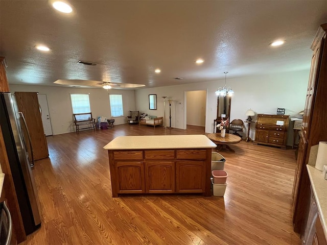 kitchen with pendant lighting, ceiling fan with notable chandelier, a textured ceiling, wood-type flooring, and stainless steel refrigerator