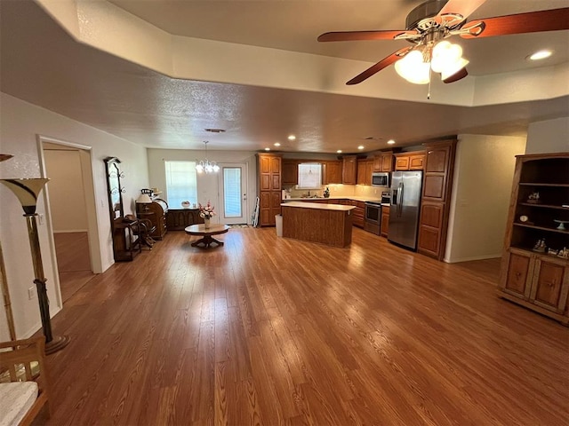 kitchen with pendant lighting, wood-type flooring, a kitchen island, ceiling fan with notable chandelier, and appliances with stainless steel finishes