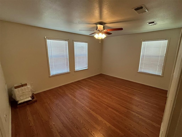 empty room with a textured ceiling, ceiling fan, a healthy amount of sunlight, and dark wood-type flooring