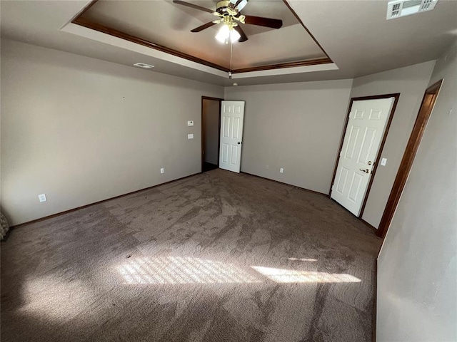 empty room with a raised ceiling, ceiling fan, crown molding, and carpet