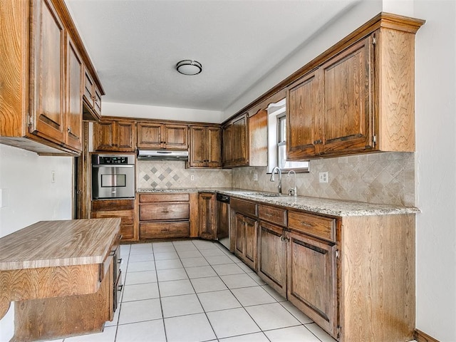 kitchen with sink, tasteful backsplash, light stone counters, light tile patterned flooring, and appliances with stainless steel finishes