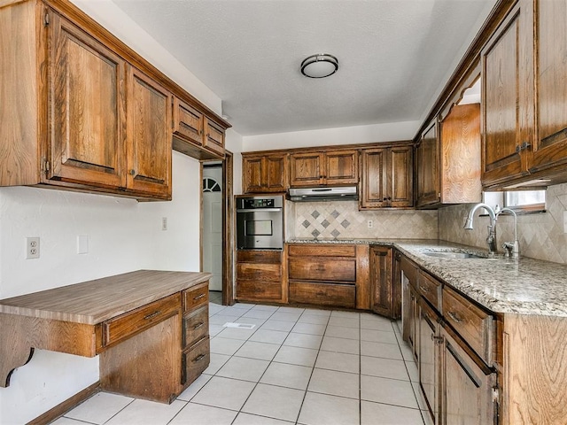 kitchen featuring tasteful backsplash, stainless steel oven, light tile patterned flooring, and sink