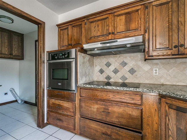 kitchen featuring decorative backsplash, black electric stovetop, light tile patterned floors, dark stone countertops, and oven