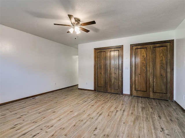 unfurnished bedroom featuring multiple closets, ceiling fan, a textured ceiling, and light wood-type flooring