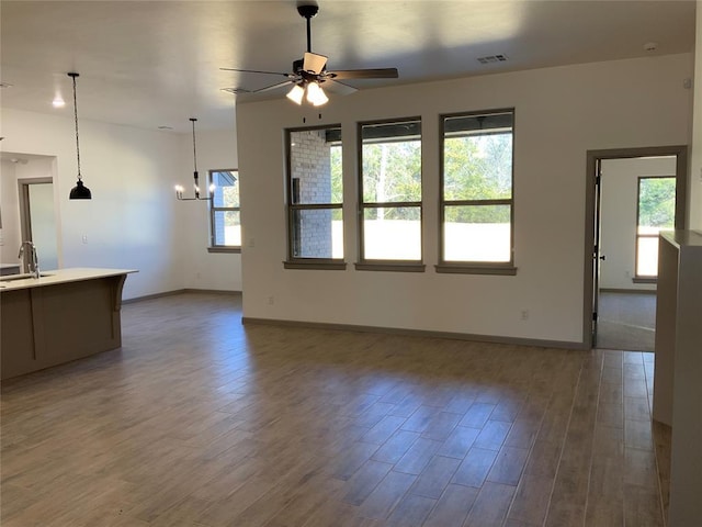 unfurnished living room with hardwood / wood-style floors, ceiling fan with notable chandelier, and sink