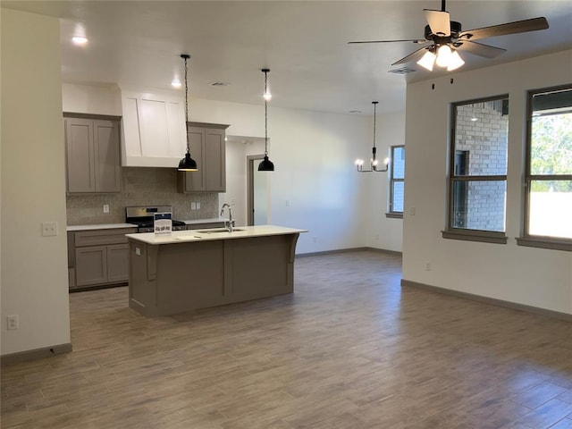 kitchen with gray cabinets, pendant lighting, sink, stainless steel range, and a center island with sink