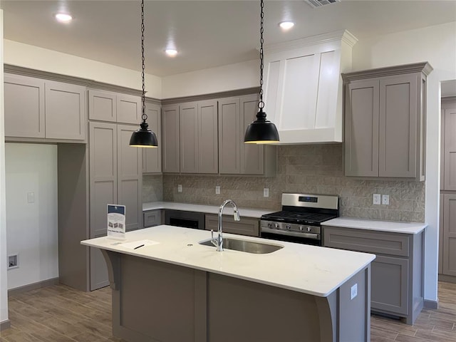 kitchen with stainless steel range with gas cooktop, sink, light hardwood / wood-style floors, and a kitchen island with sink