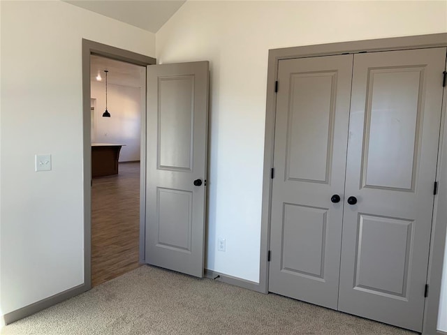 unfurnished bedroom featuring vaulted ceiling, light colored carpet, and a closet