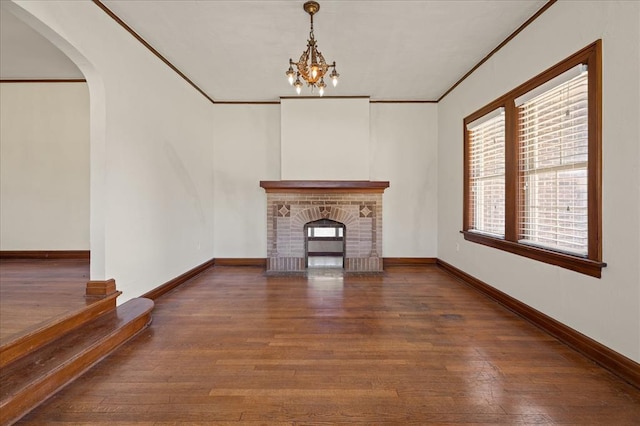 unfurnished living room featuring crown molding, a fireplace, dark hardwood / wood-style floors, and an inviting chandelier