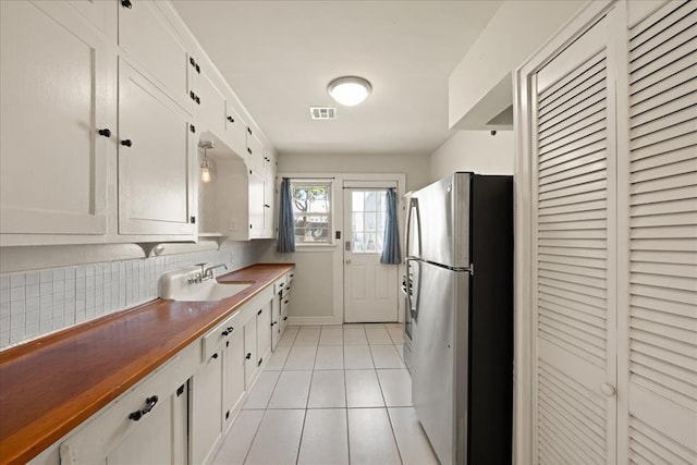 kitchen with white cabinetry, sink, butcher block countertops, stainless steel fridge, and light tile patterned floors