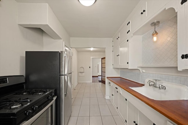 kitchen with light tile patterned flooring, sink, white cabinetry, gas stove, and butcher block counters