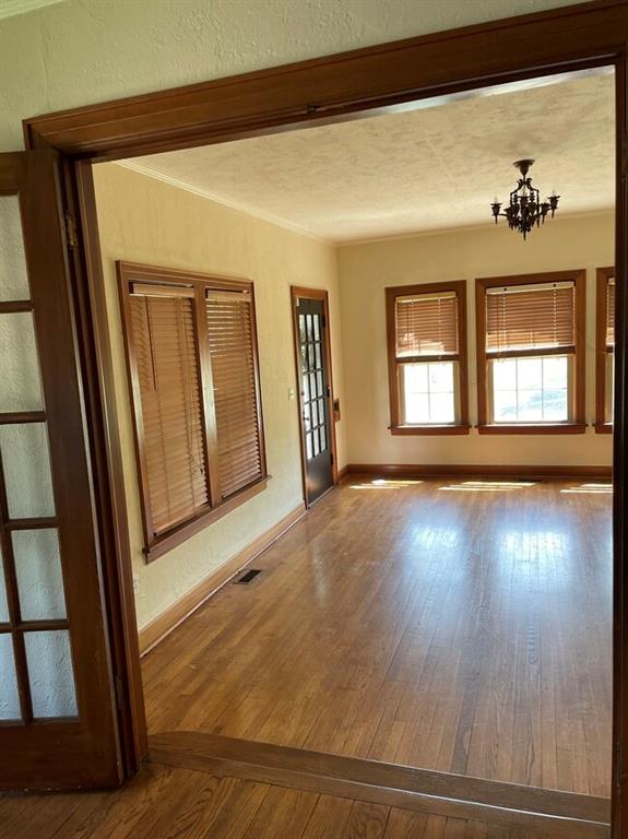 spare room featuring french doors, an inviting chandelier, wood-type flooring, a textured ceiling, and ornamental molding