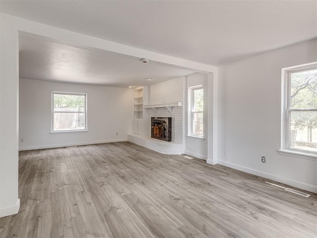 unfurnished living room featuring plenty of natural light, light hardwood / wood-style floors, built in features, and a brick fireplace